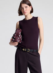 Woman wearing a purple sleeveless top and purple pants, holding a matching handbag against a light background