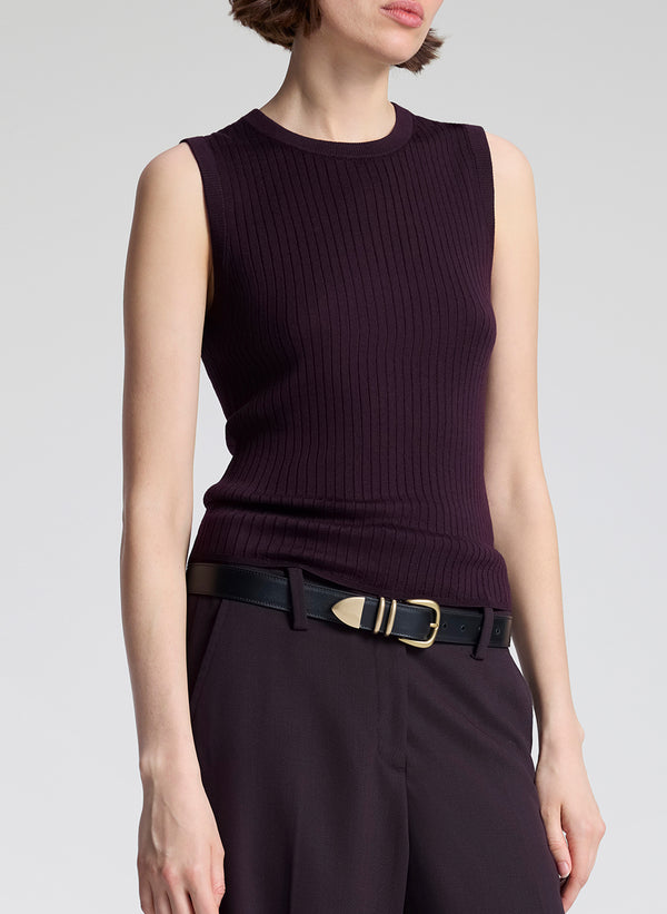 Woman wearing a purple sleeveless top and purple pants, holding a matching handbag against a light background