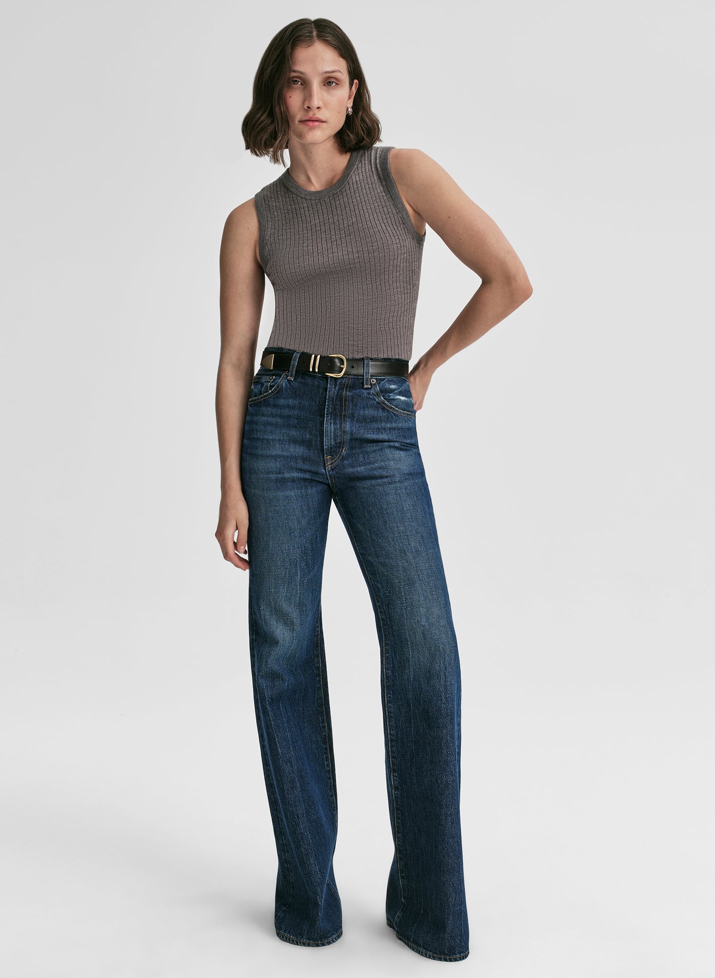 Woman wearing a gray sleeveless top and blue jeans on a light gray background
