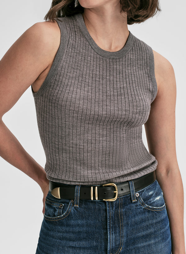 Person wearing a gray ribbed tank top and blue jeans with a white background