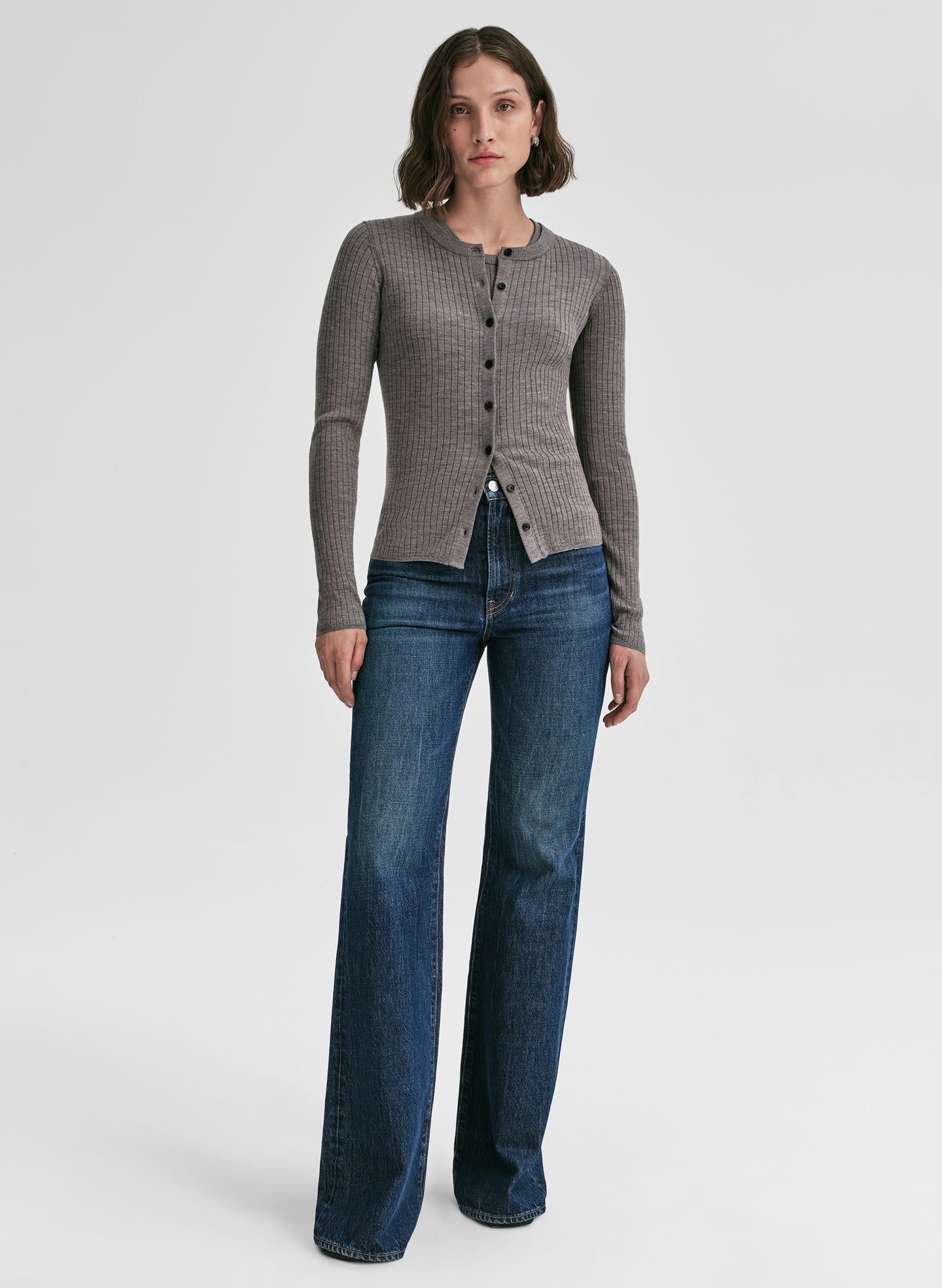 Woman wearing a grey cardigan and blue jeans on a white background