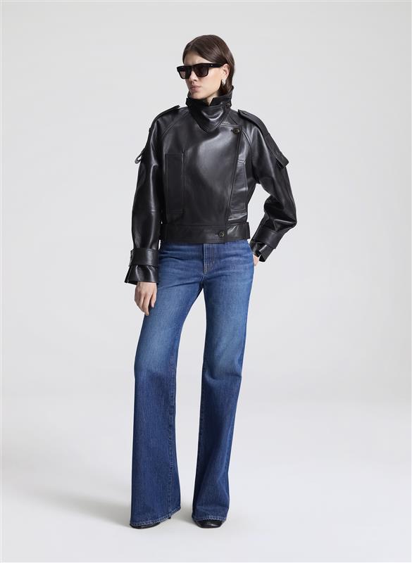 Woman wearing a dark brown leather jacket, black shirt, and blue jeans on a light gray background