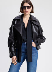 Woman wearing a dark brown leather jacket, black shirt, and blue jeans on a light gray background