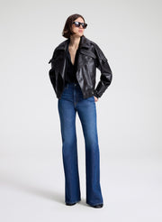 Woman wearing a dark brown leather jacket, black shirt, and blue jeans on a light gray background