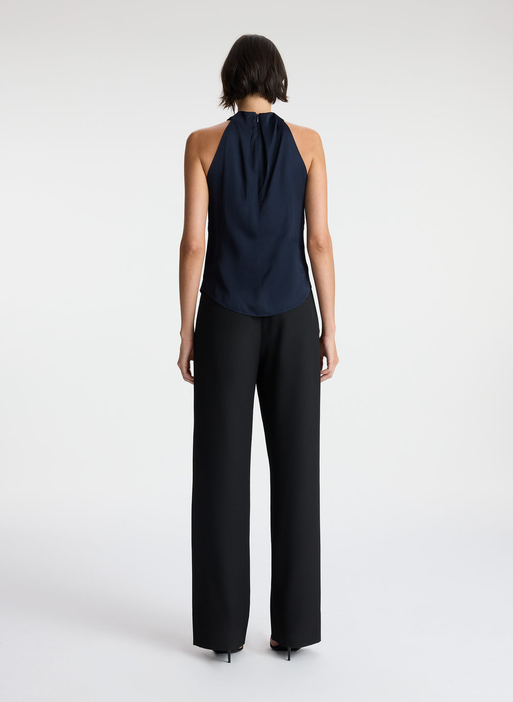 back view of woman wearing navy blue satin halter top with black pants