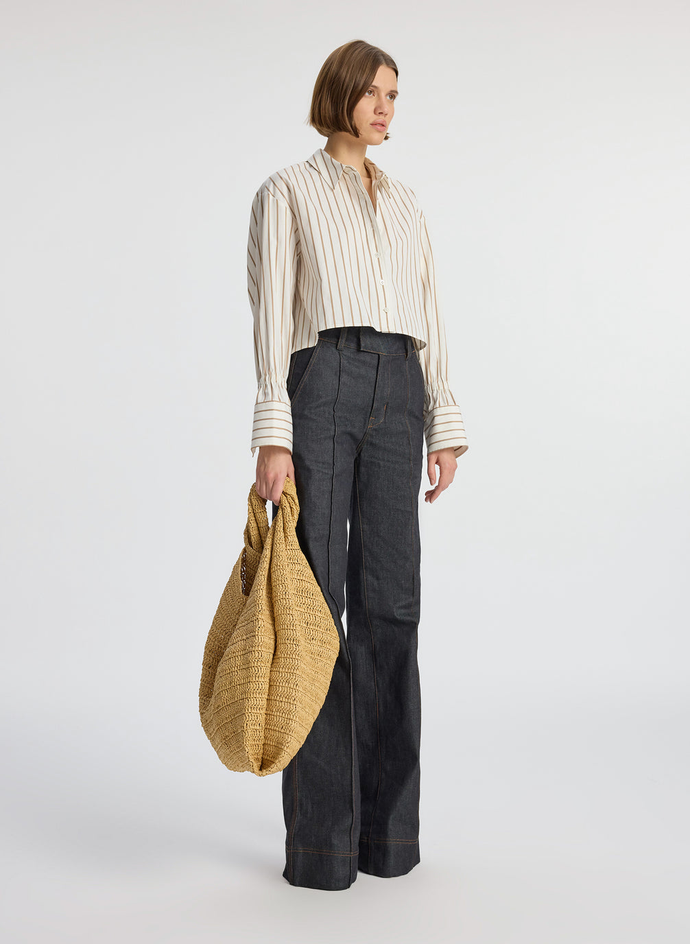 side view of woman wearing cream and brown striped collared shirt and dark wash raw denim jeans