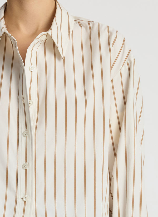 detail view of woman wearing cream and brown striped collared shirt and dark wash raw denim jeans