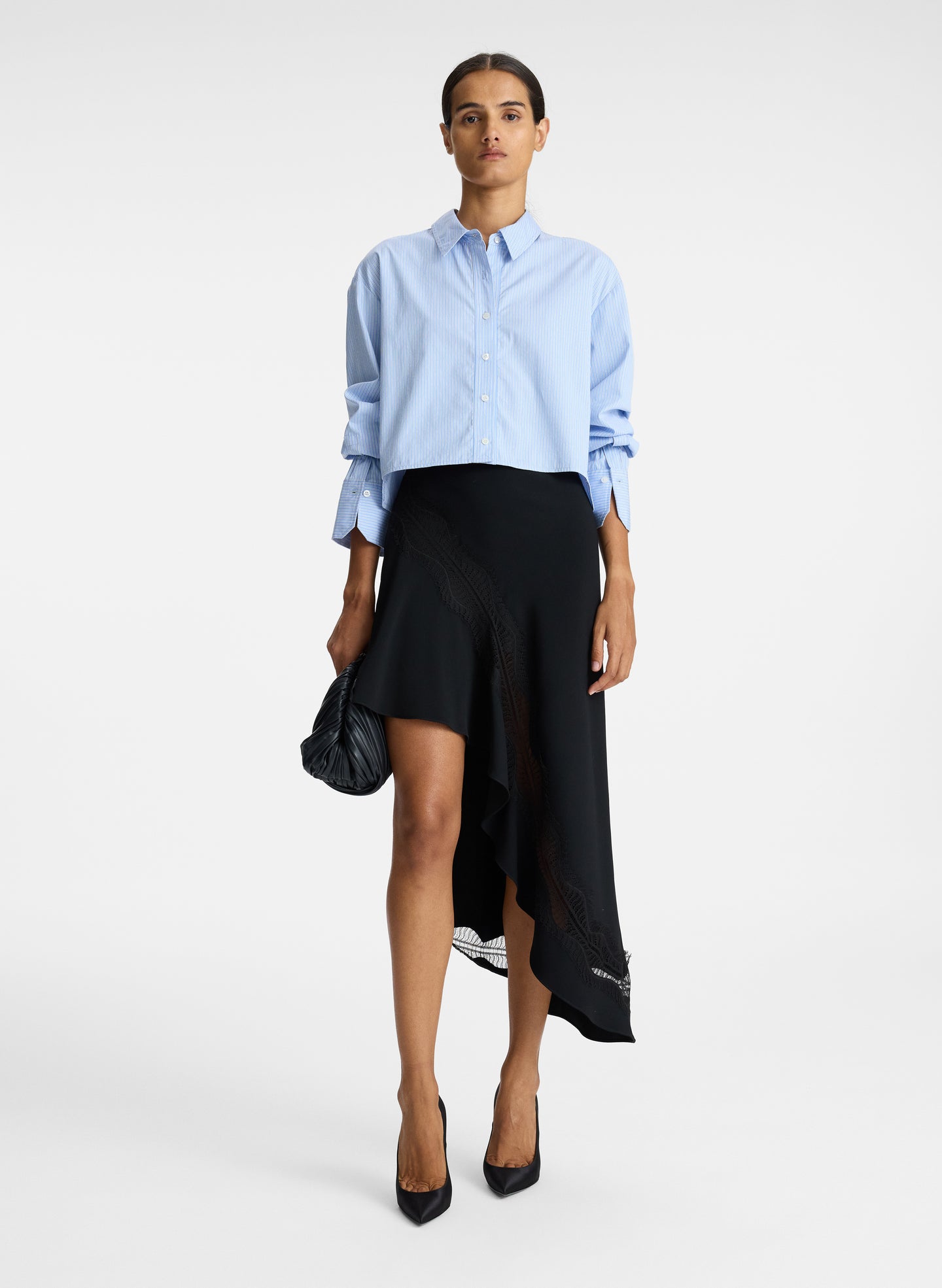 front view of woman wearing blue striped button down collared shirt and asymmetric black satin and lace skirt