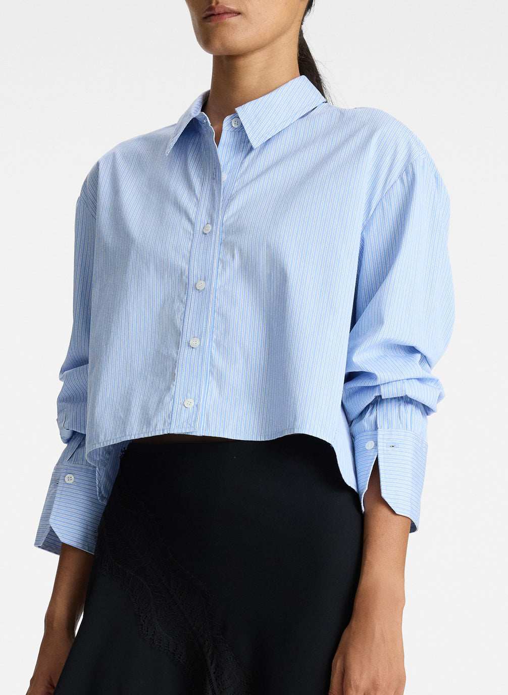 detail view of woman wearing light blue striped oversized cropped button down shirt and black asymmetric midi skirt
