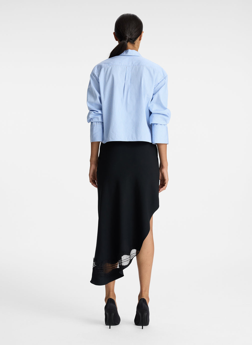 back view of woman wearing blue striped button down collared shirt and asymmetric black satin and lace skirt