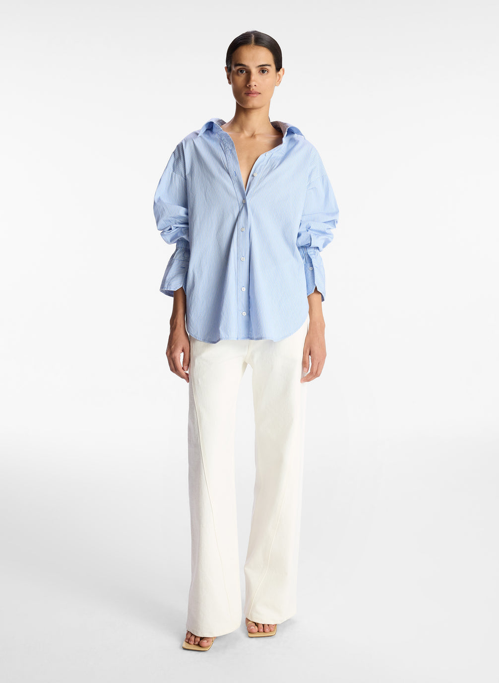 front view of woman wearing light blue striped oversized button down shirt and white pants