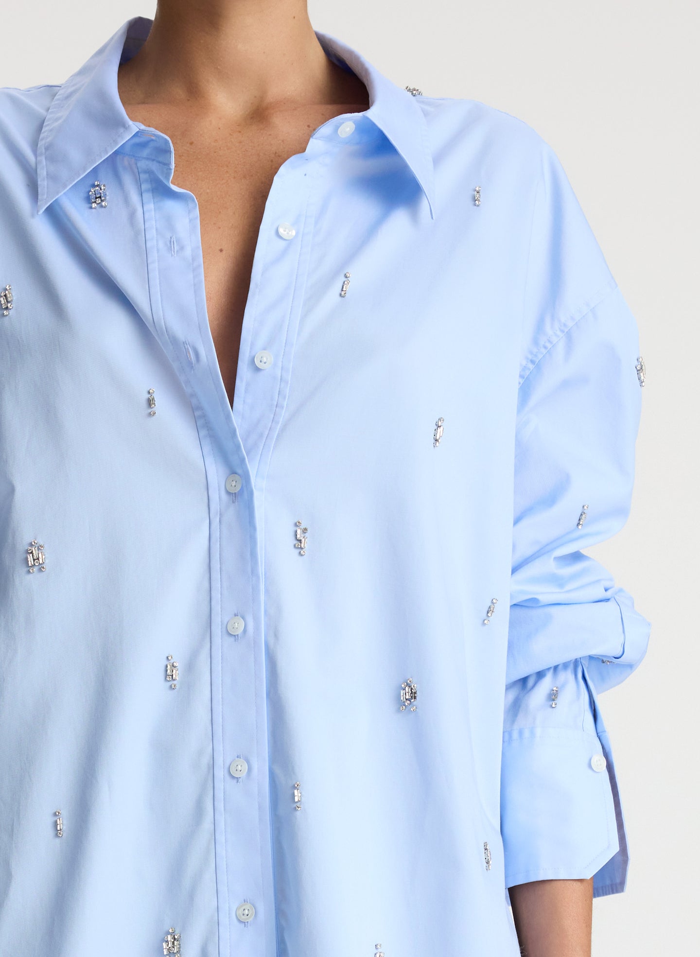 detail view of woman wearing light blue embellished oversized button down shirt and black pants