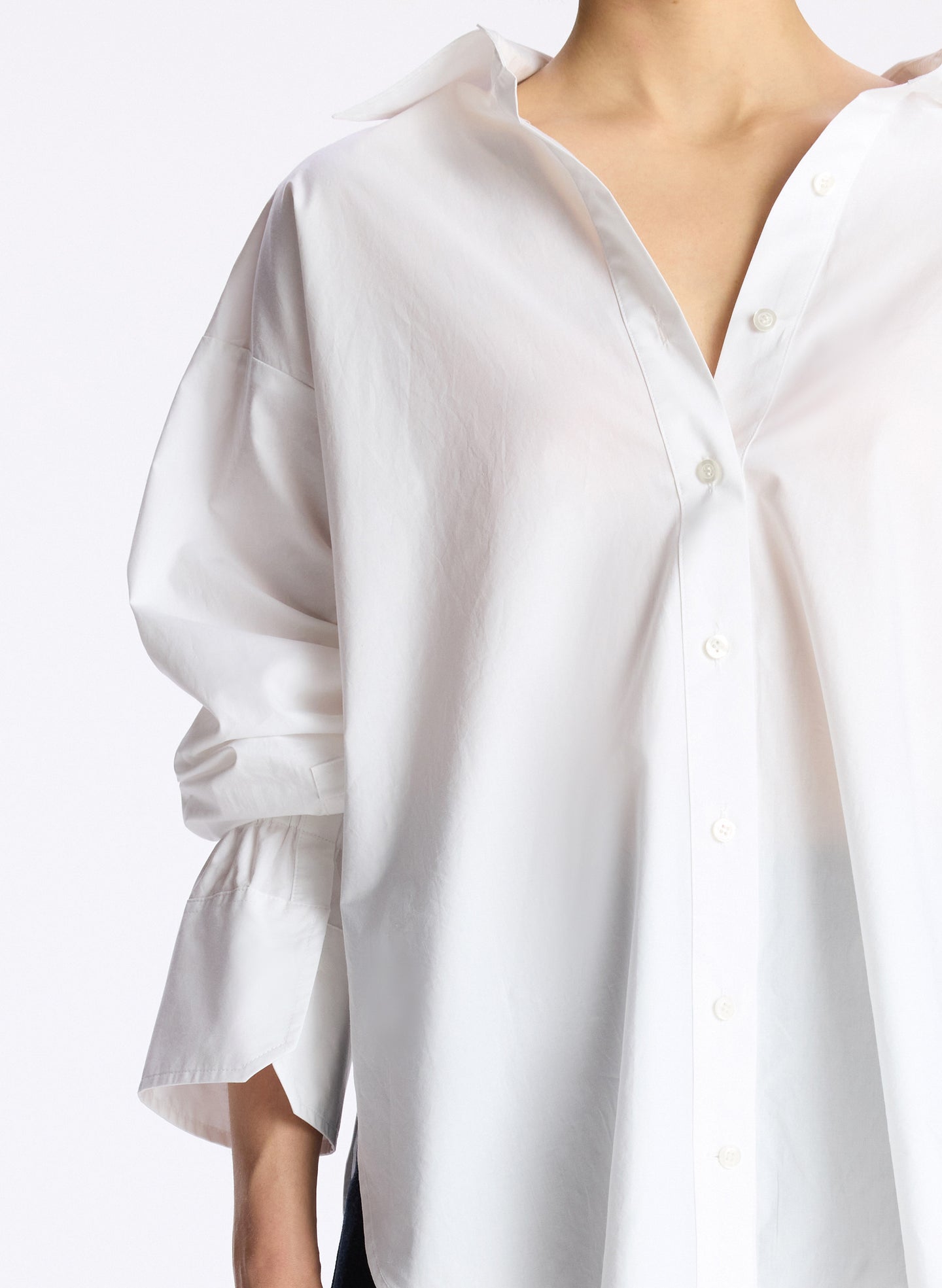 detail view of woman wearing white oversized button down shirt and dark wash denim jeans