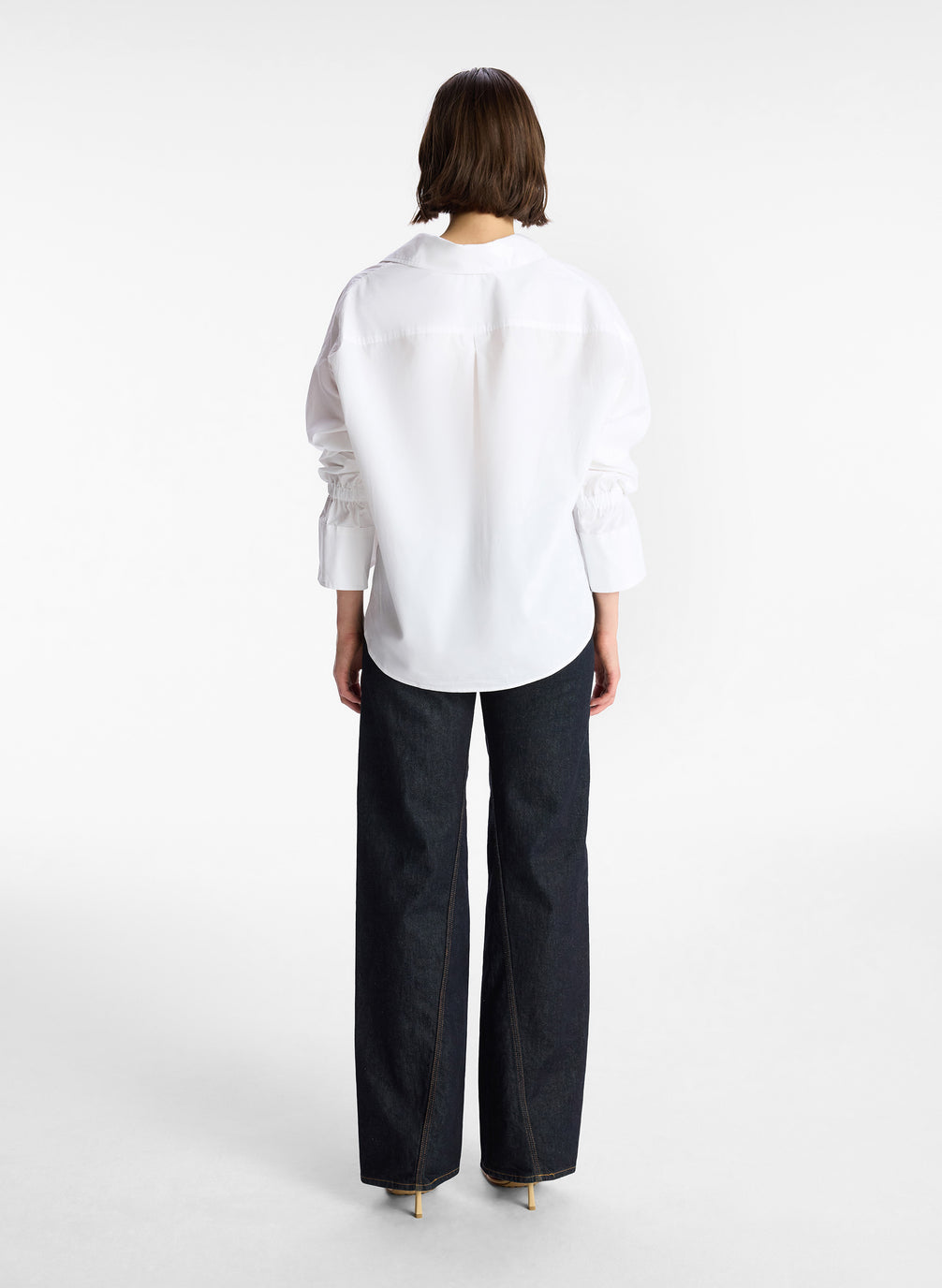 back view of woman wearing white oversized button down shirt and dark wash denim jeans