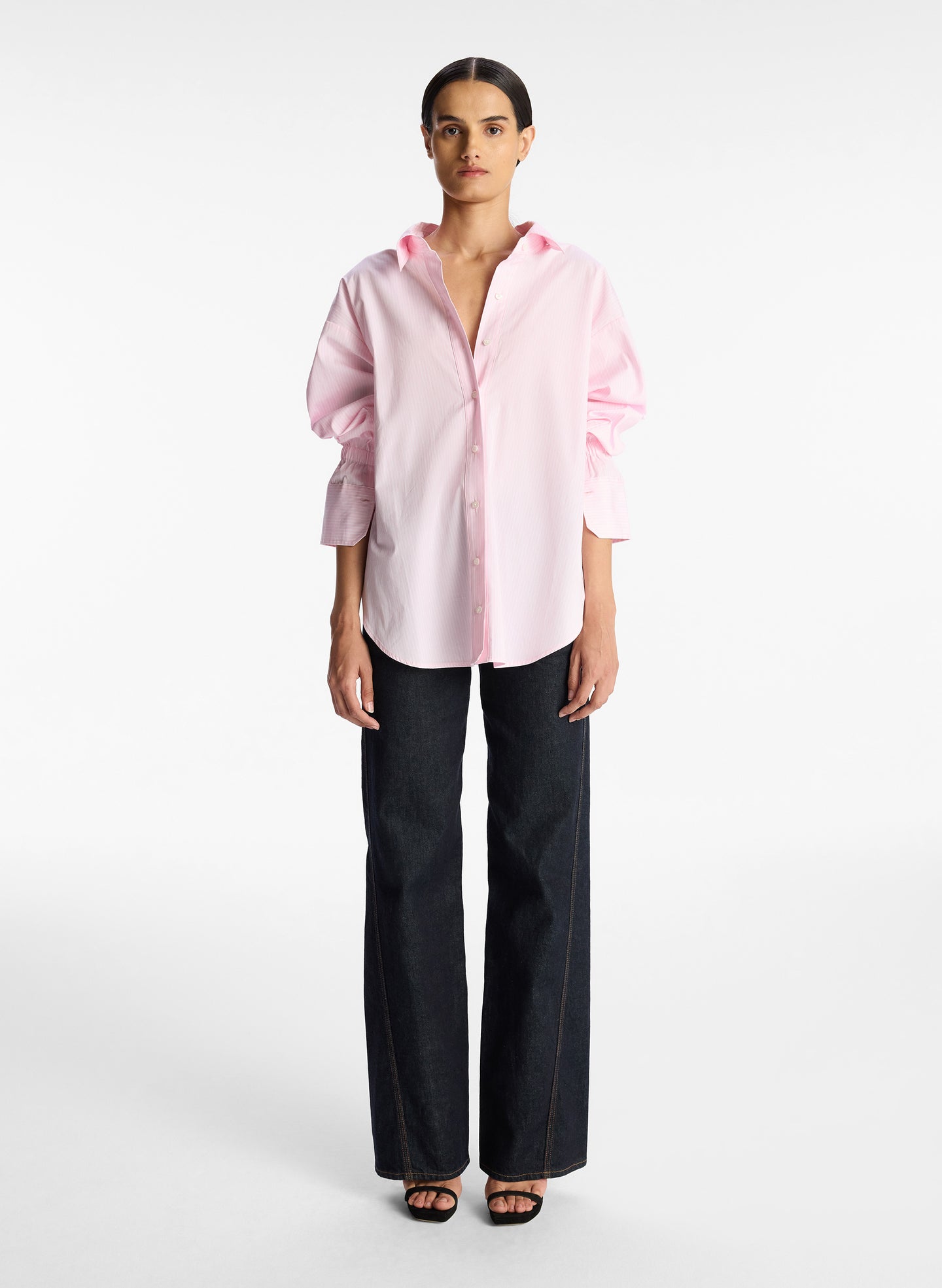 front view of woman wearing pink striped oversized button down shirt and dark wash denim jeans