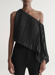 Woman wearing a black pleated one-shoulder top and black pants against a plain background