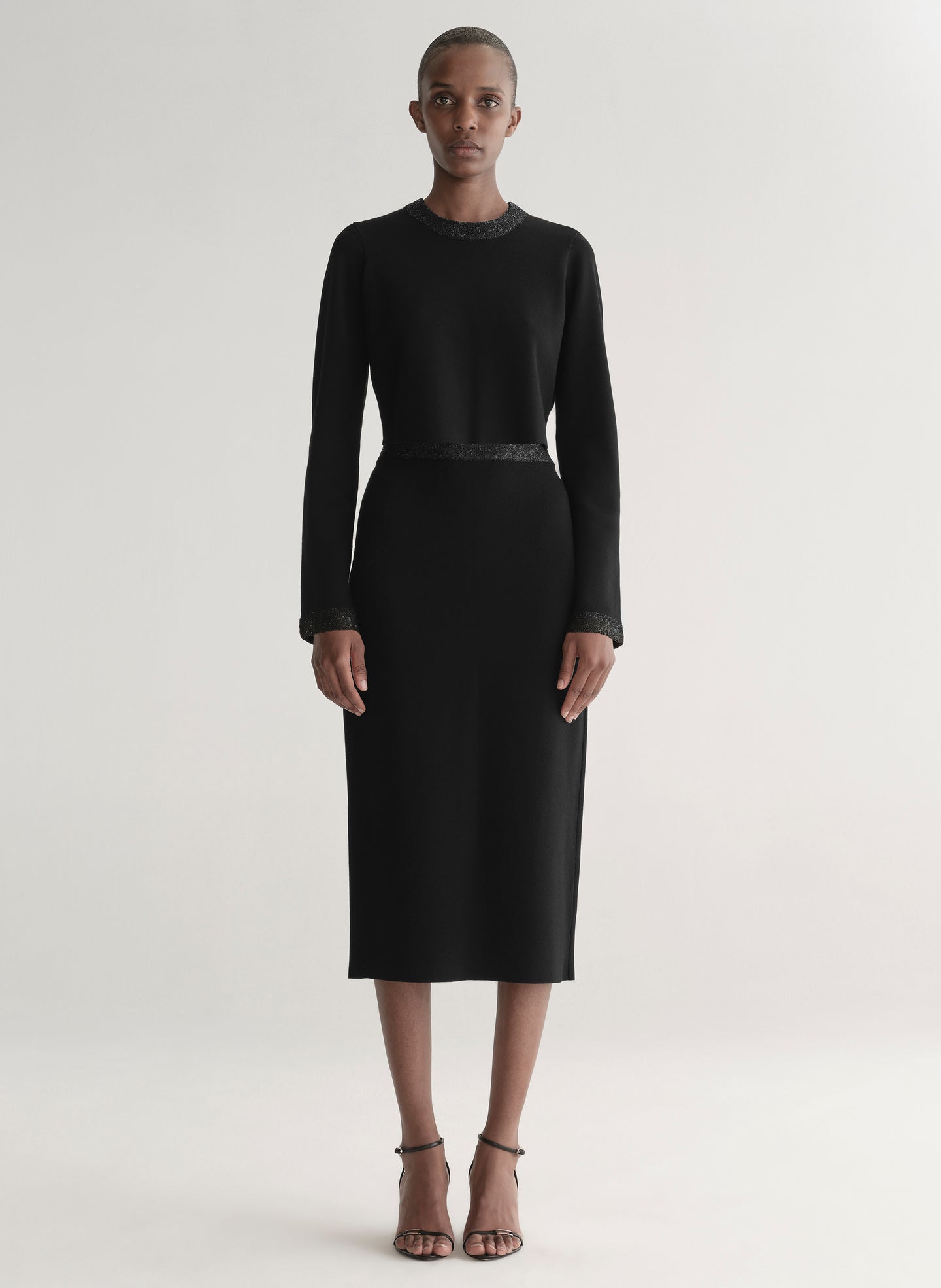 Woman wearing a black outfit with textured details on a plain background