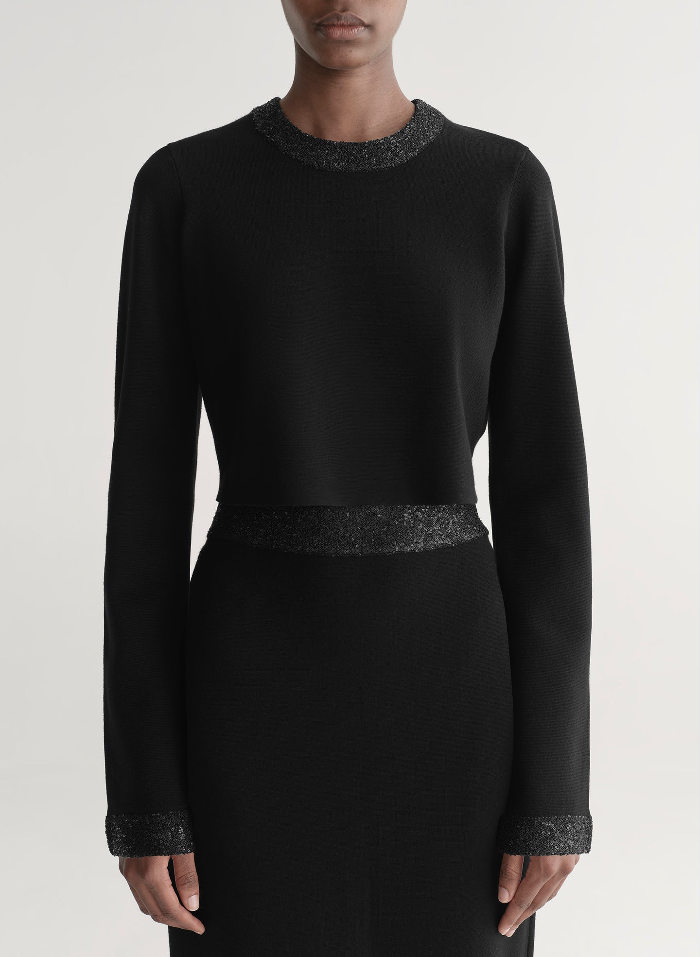 Woman wearing a black outfit with textured details on a plain background