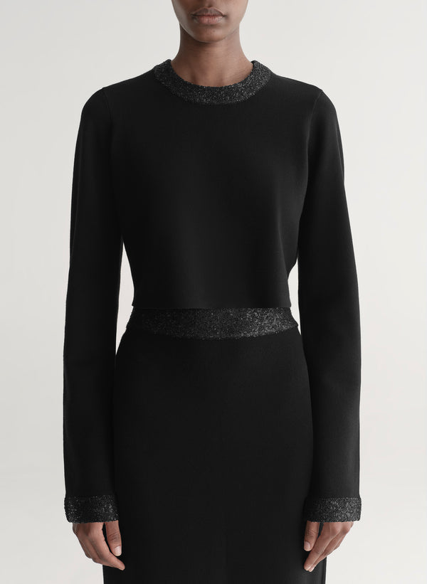 Woman wearing a black outfit with textured details on a plain background