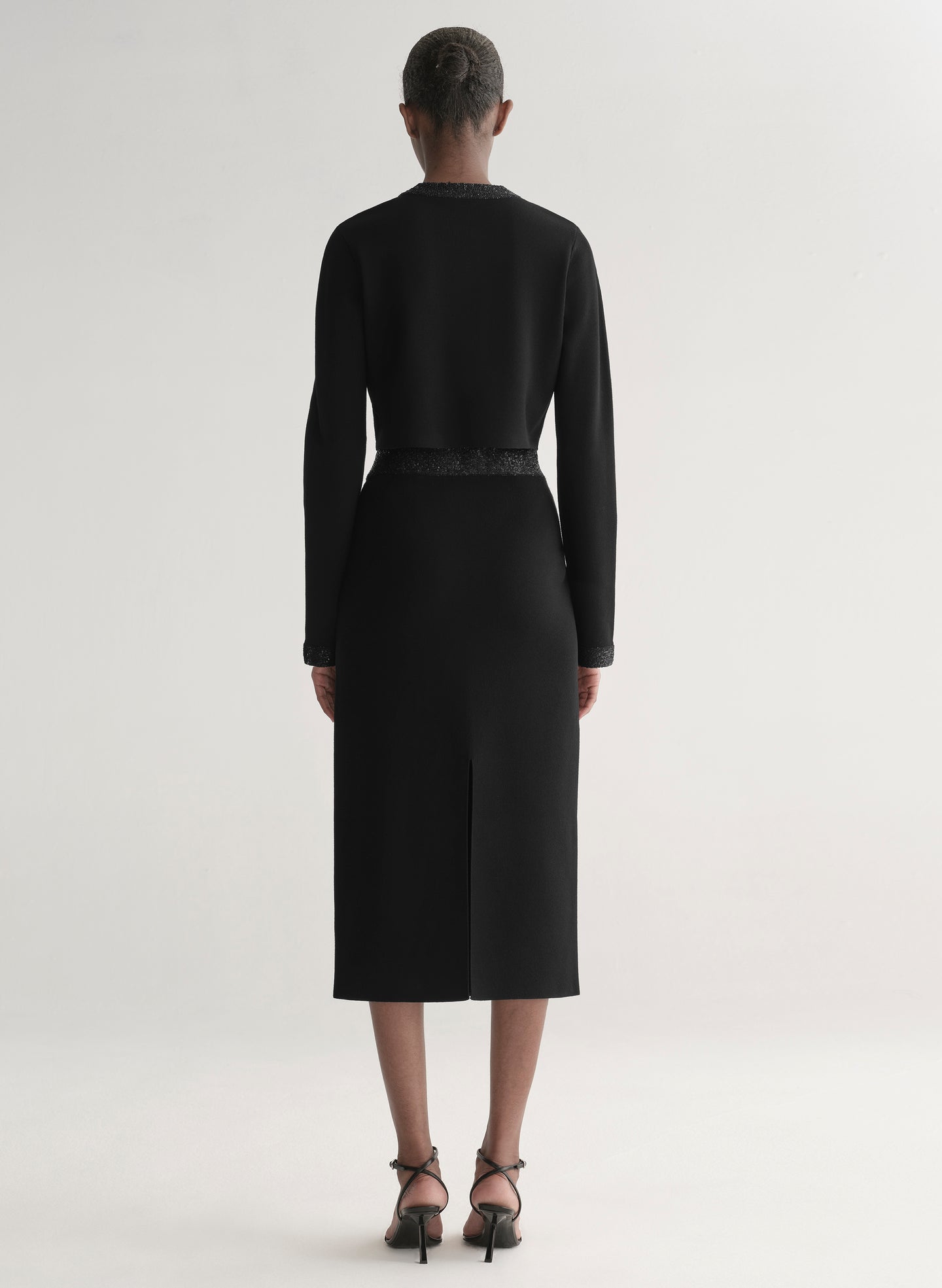 Woman wearing a black outfit with textured details on a plain background