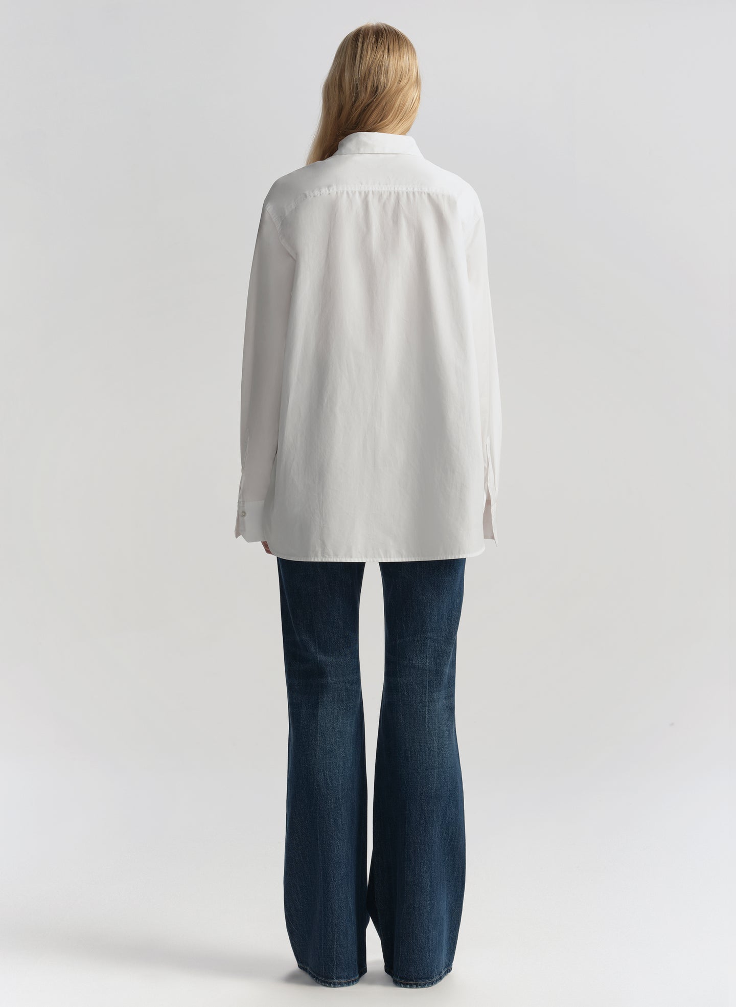 Woman wearing a white shirt and blue jeans on a plain background