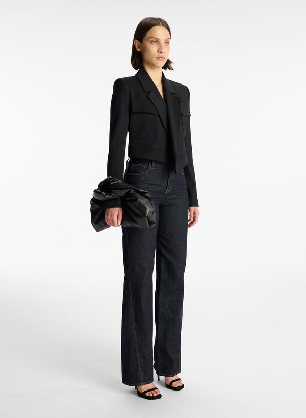 flat lay view of woman wearing black vegan leather short length top handle bag with small sized rectangular base