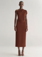 Woman wearing a rust one shoulder knit top and matching skirt against a plain background