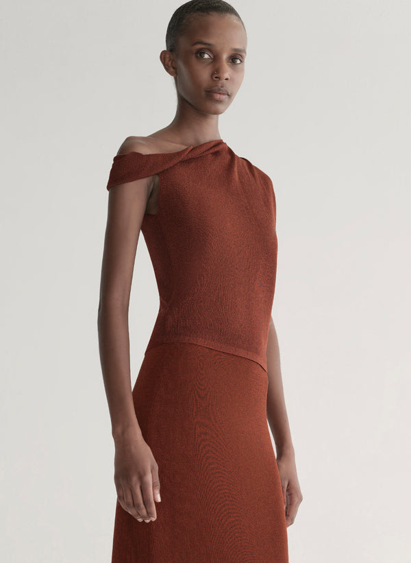 Woman wearing a rust one shoulder knit top and matching skirt against a plain background