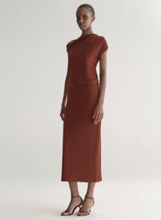 Woman wearing a rust one shoulder knit top and matching skirt against a plain background