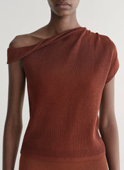 Woman wearing a rust one shoulder knit top and matching skirt against a plain background