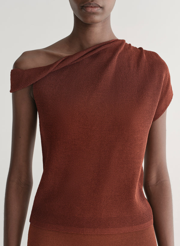 Woman wearing a rust one shoulder knit top and matching skirt against a plain background