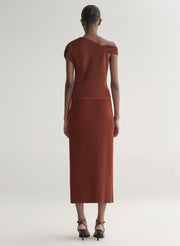 Woman wearing a rust one shoulder knit top and matching skirt against a plain background