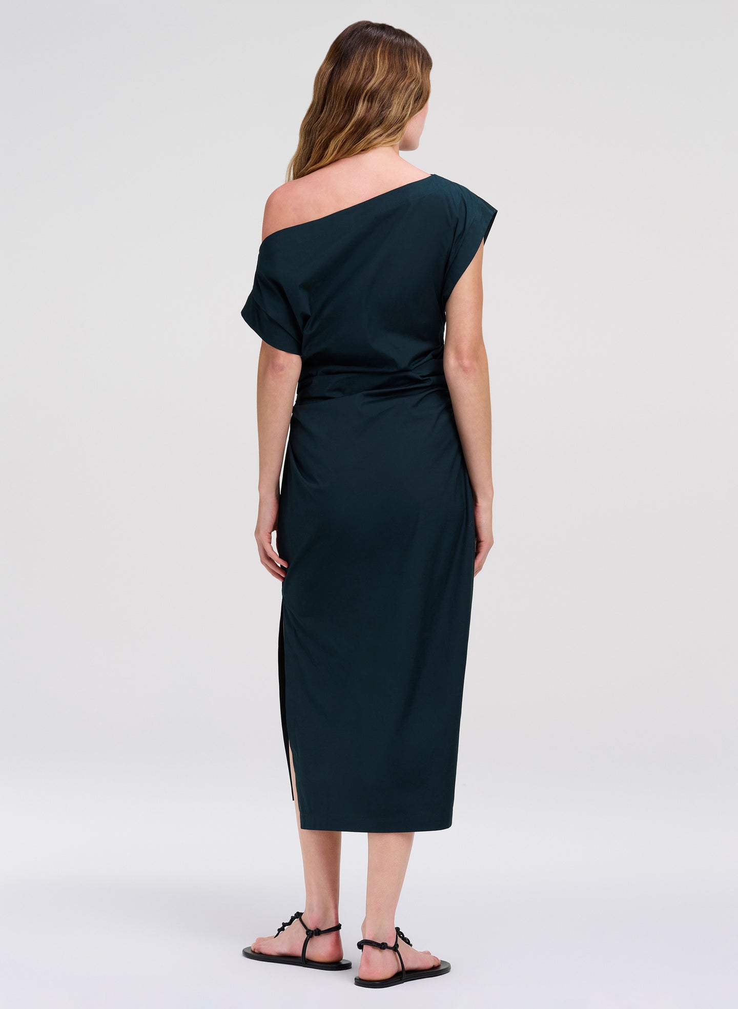 Woman wearing a dark teal one-shoulder dress on a white background