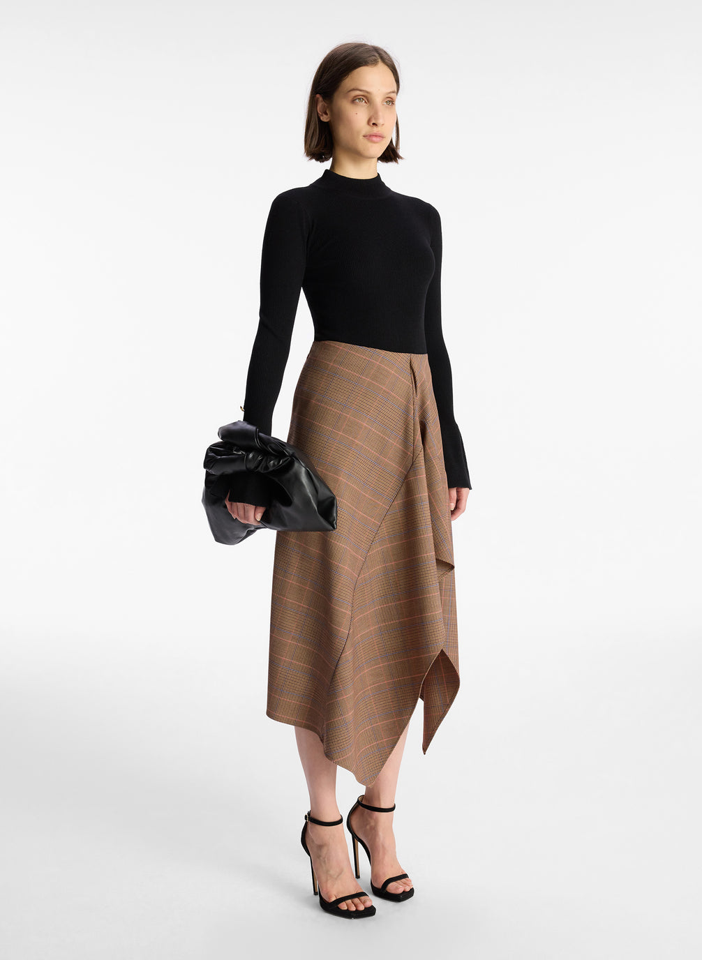 side  view of woman wearing black sweater and brown plaid asymmetric midi skirt