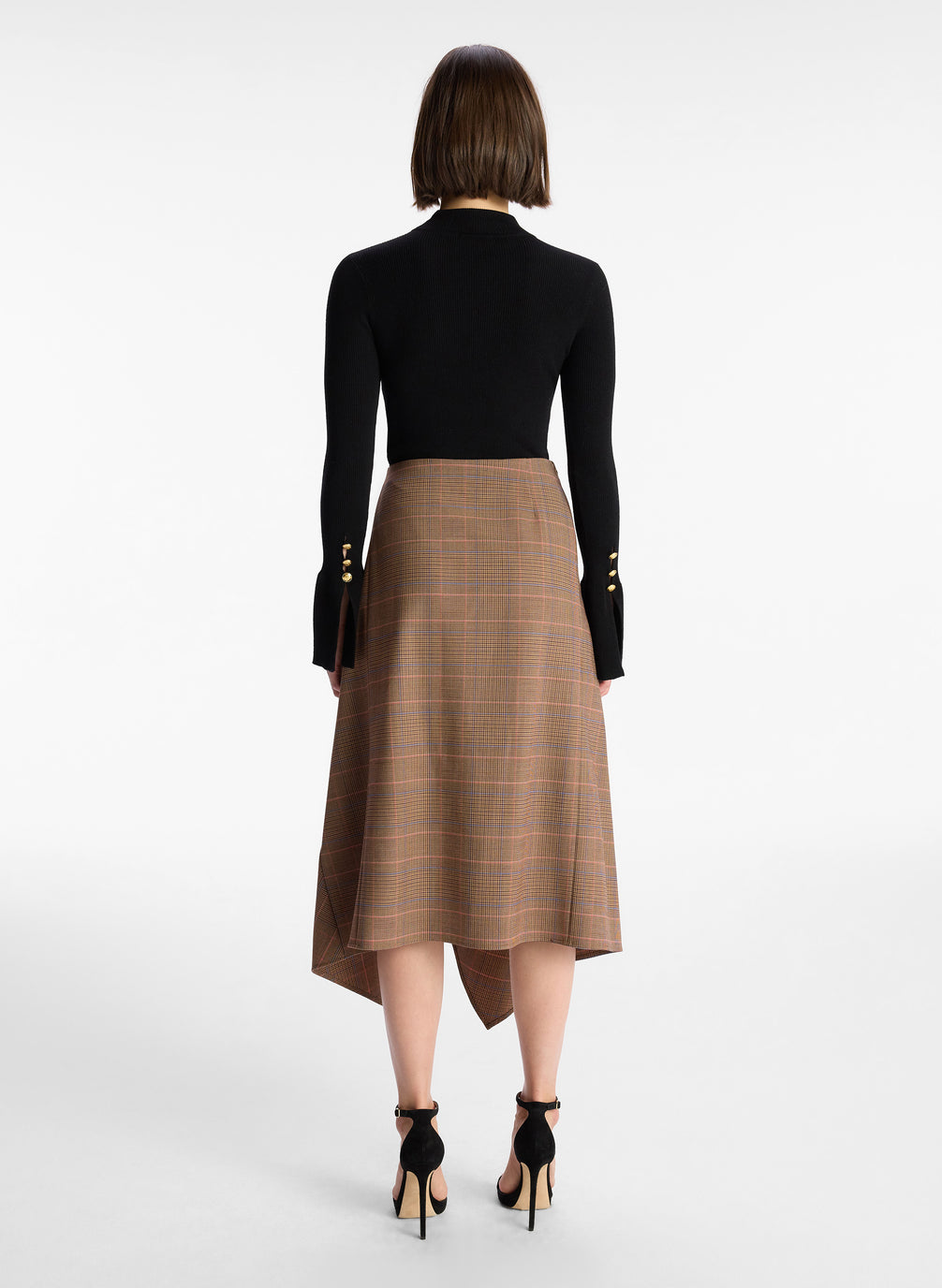 back  view of woman wearing black sweater and brown plaid asymmetric midi skirt