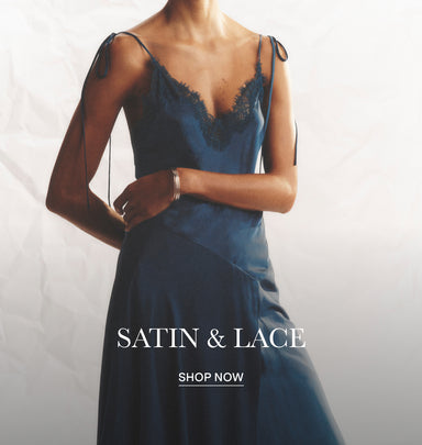 A woman wearing a satin slip dress with black lace trim at the neckline and thin shoulder ties, posed against a light gray textured background with the text 'SATIN & LACE' and 'SHOP NOW' overlaid.