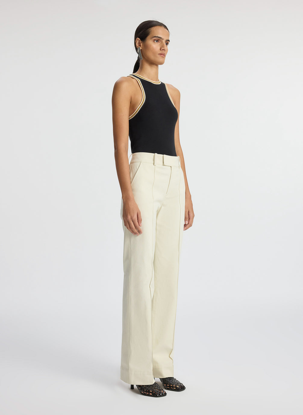side view of woman wearing black tank top with contrast trim and cream pants