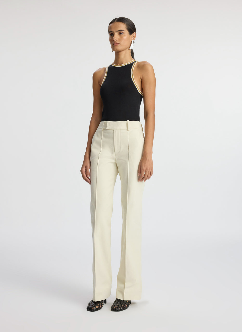 side view of woman wearing black tank top with contrast trim and cream pants