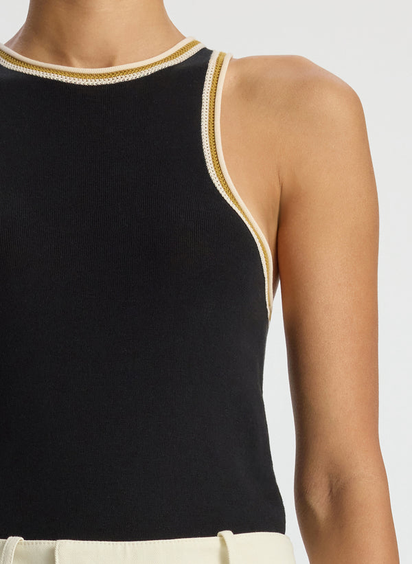 detail view of woman wearing black tank top with contrast trim and cream pants