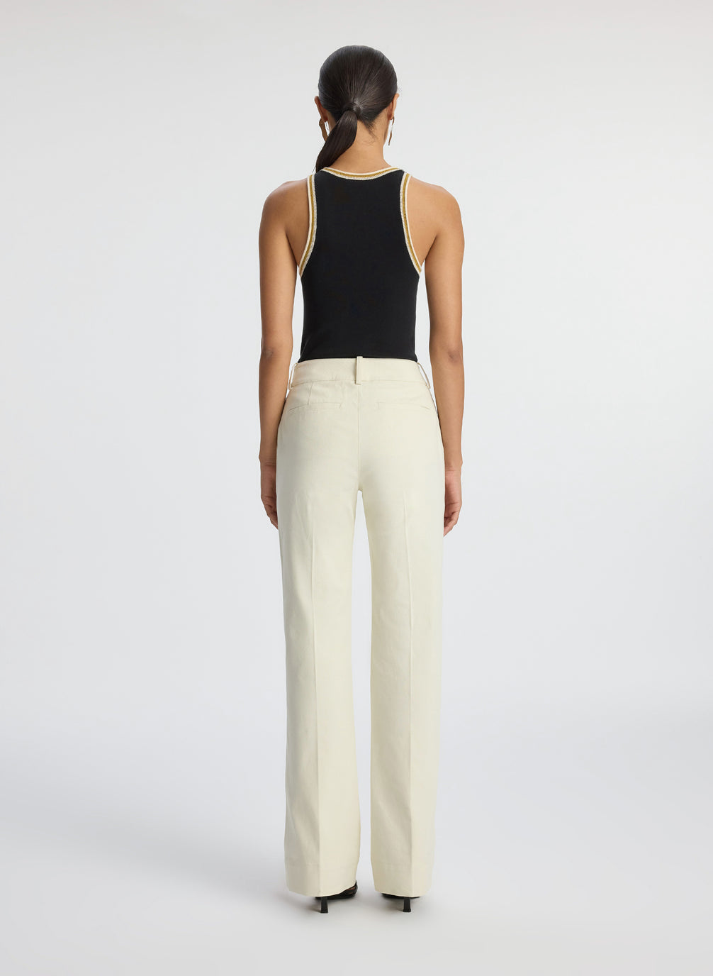 back view of woman wearing black tank top with contrast trim and cream pants