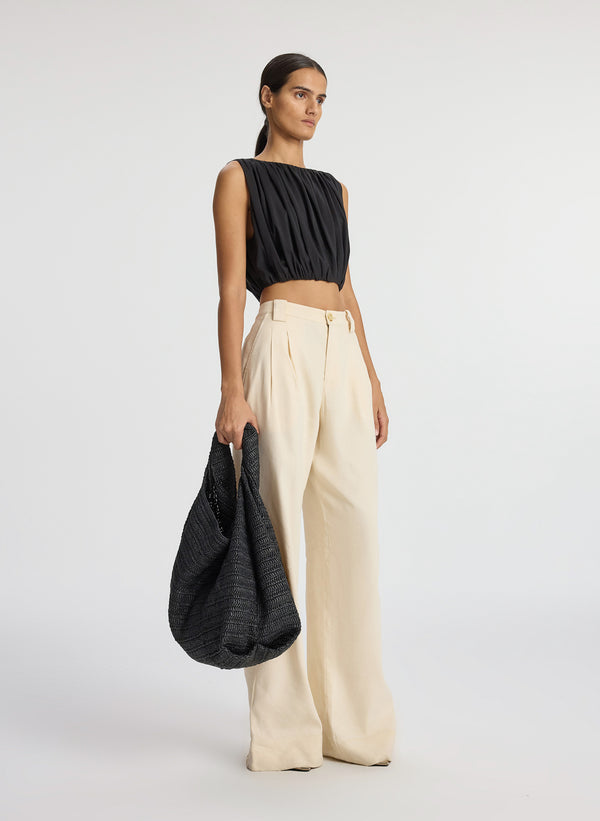 side view of woman wearing black sleeveless cropped top and beige wide leg pants