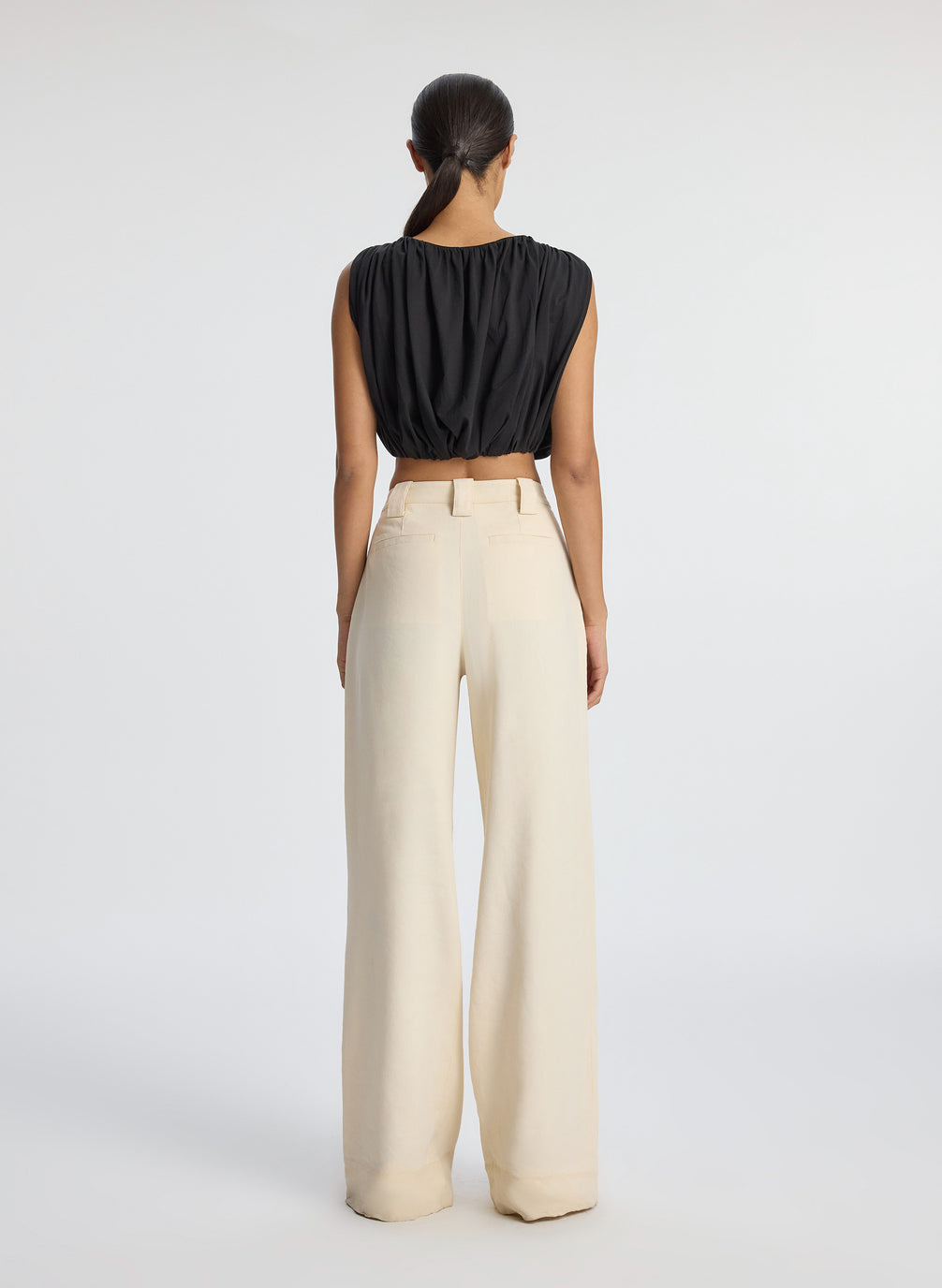 back view of woman wearing black sleeveless cropped top and beige wide leg pants