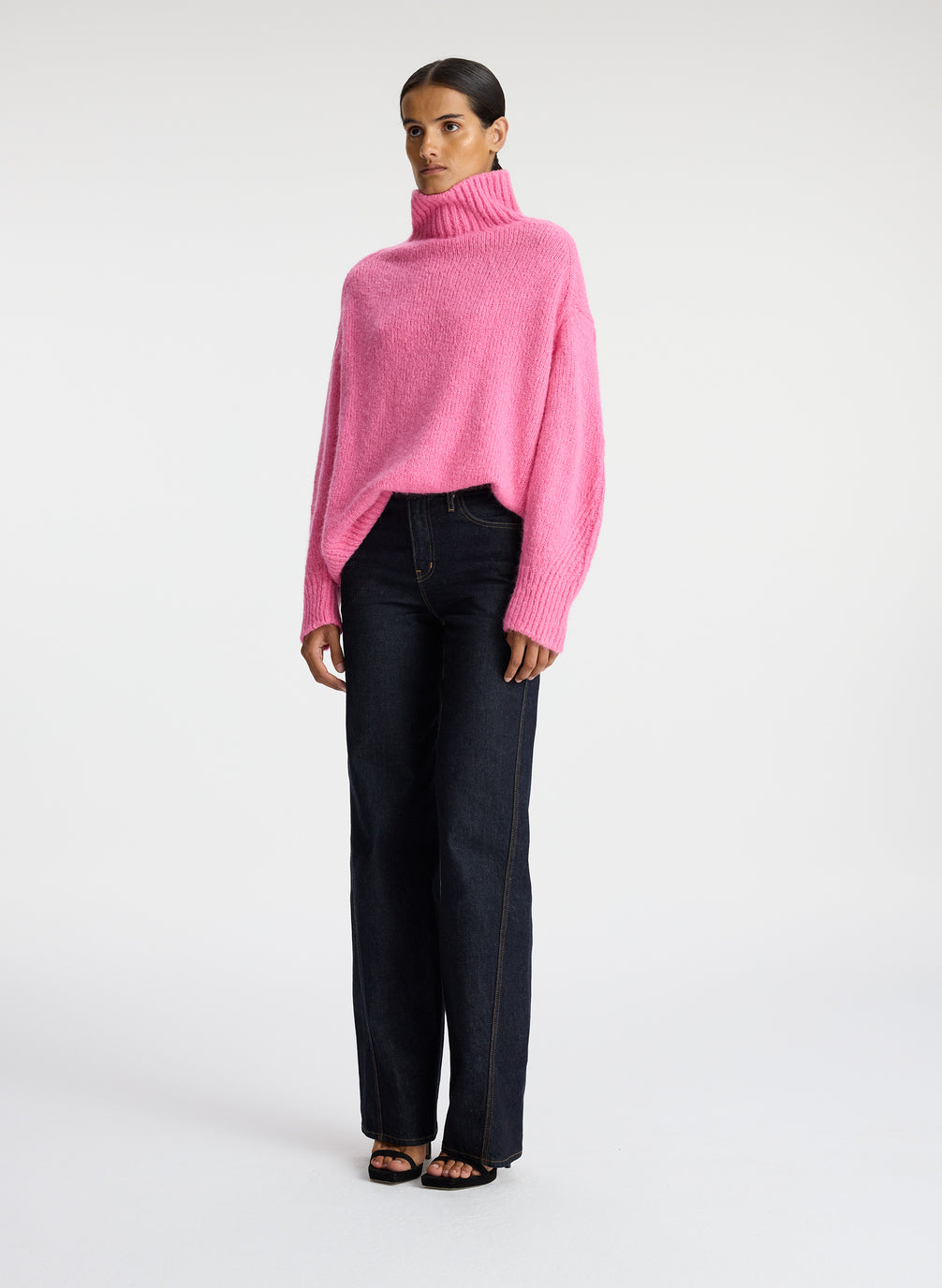 side view of woman wearing pink turtleneck sweater and dark wash denim jeans