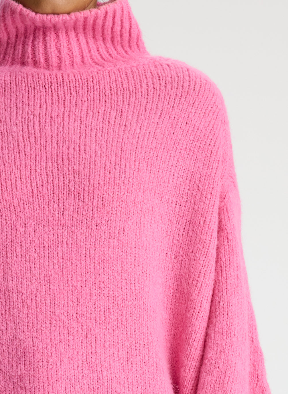 detail view of woman wearing pink turtleneck sweater and dark wash denim jeans