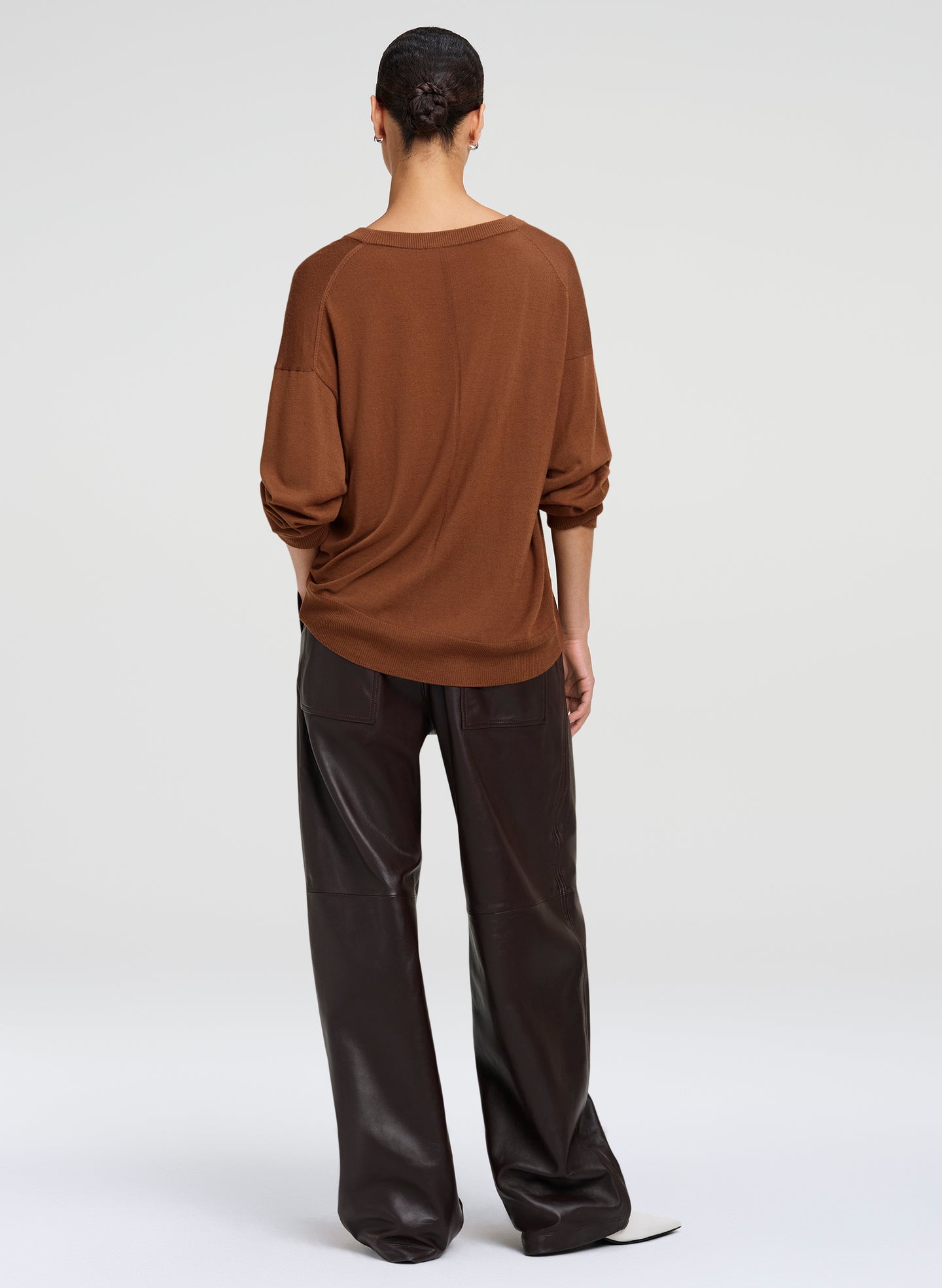 A model shown from the back wearing a brown long-sleeve top and brown wide-leg pants against a light gray studio background.