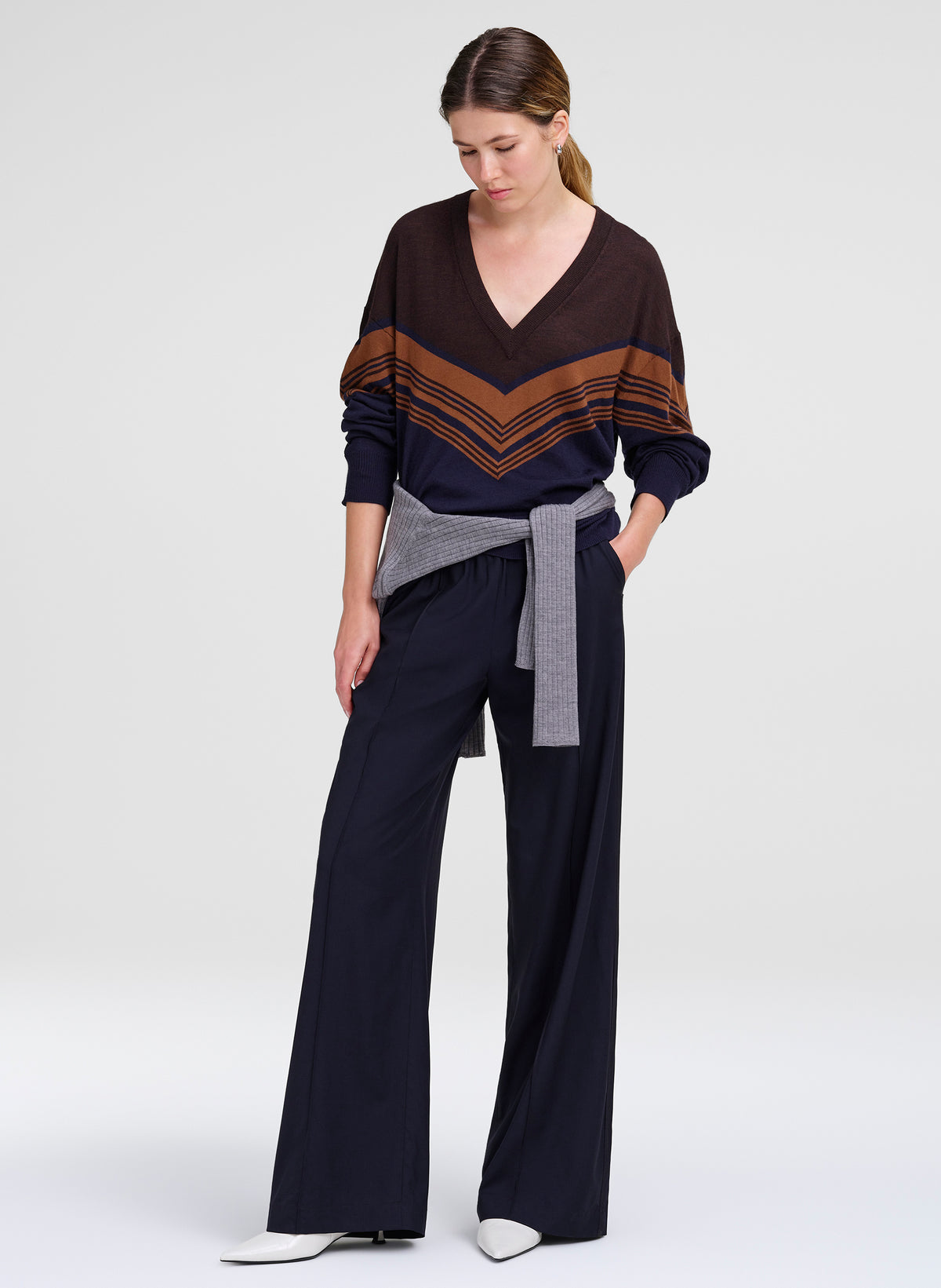 woman wearing chevron striped sweater, grey sweater tied at waist, and blue pants