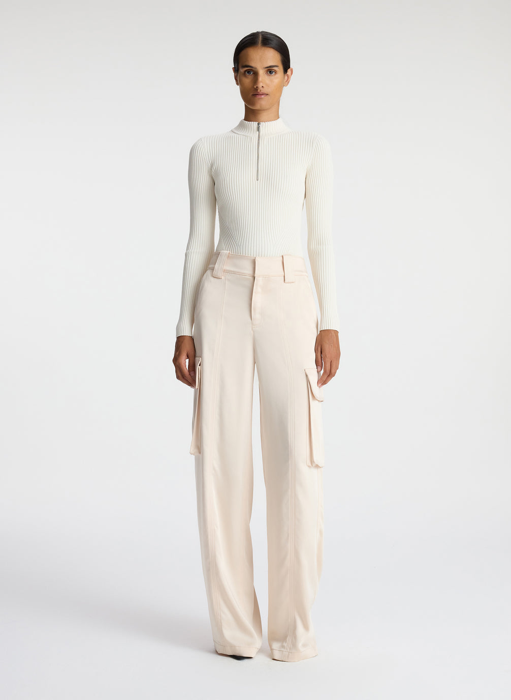 front view of woman wearing white half zip mock neck long sleeve knit top and off white satin cargo pants