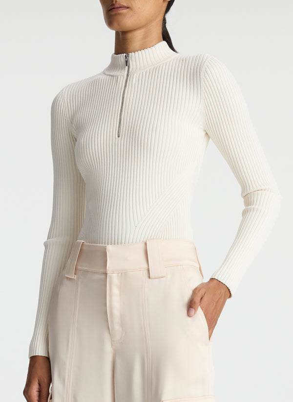 detail view of woman wearing white half zip mock neck long sleeve knit top and off white satin cargo pants