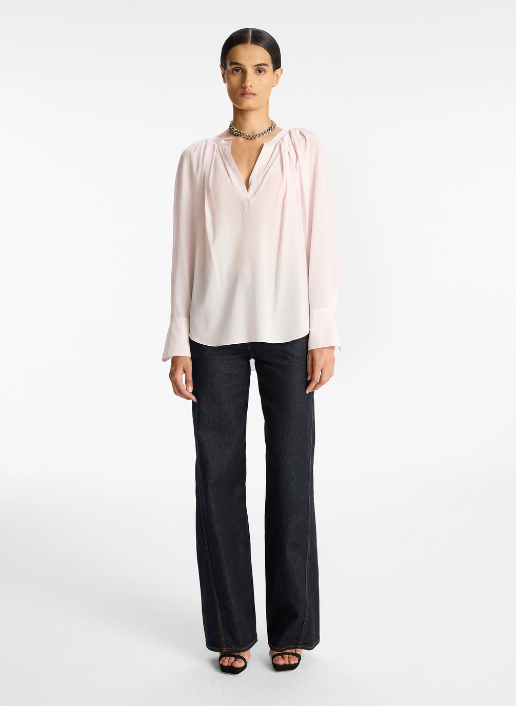 front view of woman wearing light pink v neck long sleeve silk top and dark wash denim jeans