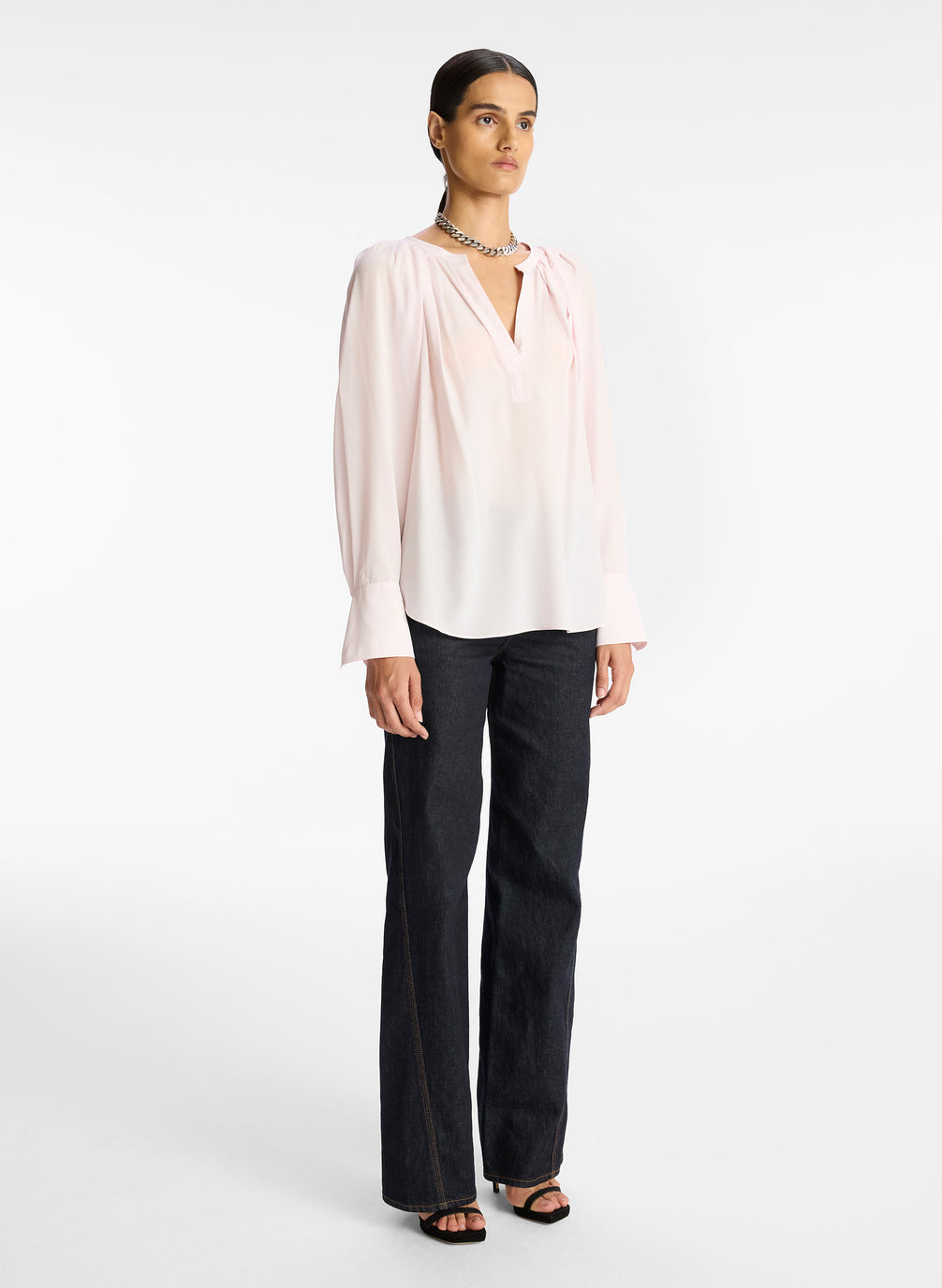 side view of woman wearing light pink v neck long sleeve silk top and dark wash denim jeans